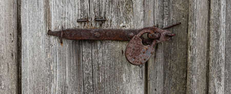 Close up view of the old rusty padlock on a aged gray wooden door.