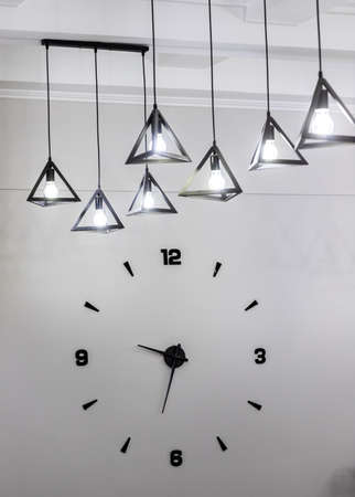 Minimalistic design of a wall clock with black numbers and a light bulb.