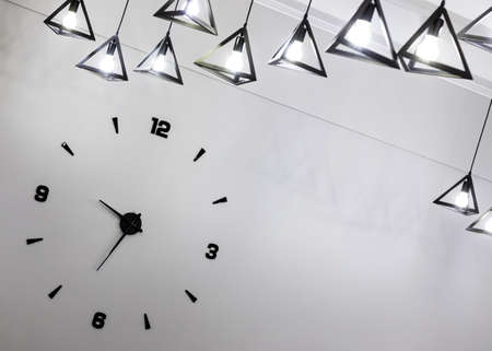 Minimalistic design of a wall clock with black numbers and a light bulb.の写真素材