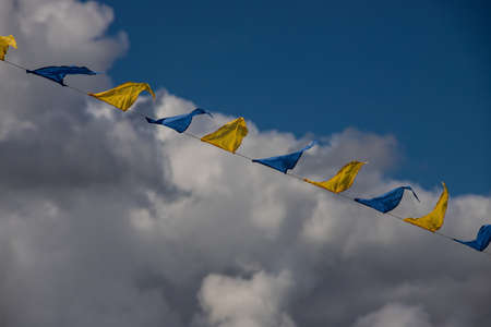 Yellow and blue triangular festival flags on sky background with white clouds. Outdoor Celebration Party. Festive moodの写真素材