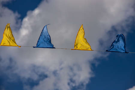 Yellow and blue triangular festival flags on sky background with white clouds. Outdoor Celebration Party. Festive moodの写真素材