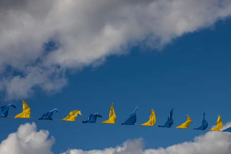 Yellow and blue triangular festival flags on sky background with white clouds. Outdoor Celebration Party. Festive moodの写真素材