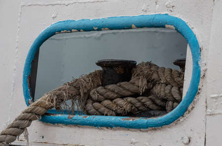 Worn old rusty mooring bollard with heavy ropes on the deck of a ship, closeup.の写真素材