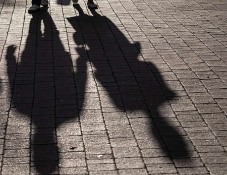 Shadows on pavement of two People walking under bright sunlight.