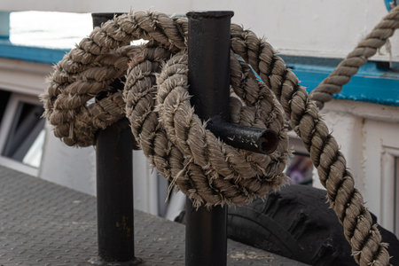 Worn old rusty mooring bollard with heavy ropes on the deck of a ship, closeup.