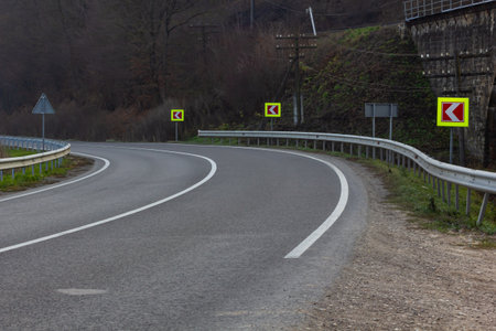 Asphalt road with bright traffic signs in situ of the sharp left turn.
