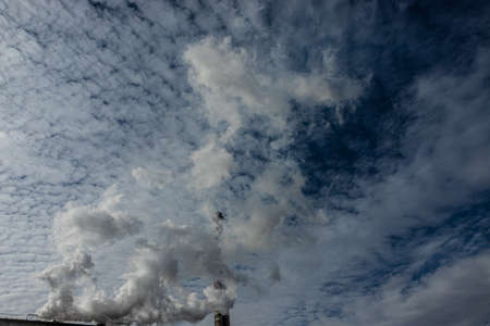 White and gray smoke and steam from a high concrete chimney against the bright blue sky.