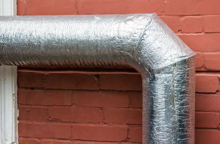 Metal ventilation pipes on the outer wall of a beige industrial building against background.