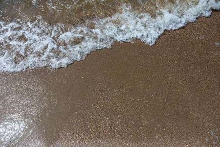 Close-up of sea foam on the sand beach with summer sunlight.