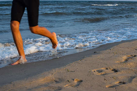 Woman is running ahead on the beach of the sea. Legs close-up.の写真素材