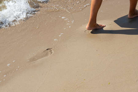 Footprints of a man on the yellow beach sand from walking barefoot by the sea with water that washes away the footprints. Contemplation of lifeの写真素材