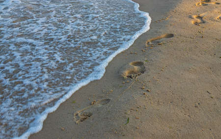Footprints of a man on the yellow beach sand from walking barefoot by the sea with water that washes...