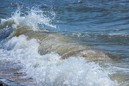 Sea waves crash against large rocks on the shore, forming large splashes..