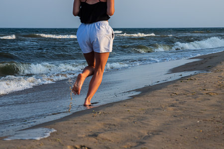 Woman is running ahead on the beach of the sea. Legs close-up.