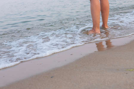 Man's bare feet stepping on calm seashore foamy wave and wet sand by evening, enjoying life and...