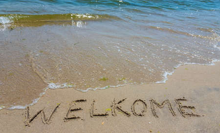 Handwriting inscription welkome word on tropical sandy beach, travel concept card for holidays.