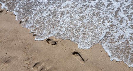 Footprints of a man on the yellow beach sand from walking barefoot by the sea with water that washes away the footprints. Contemplation of lifeの写真素材