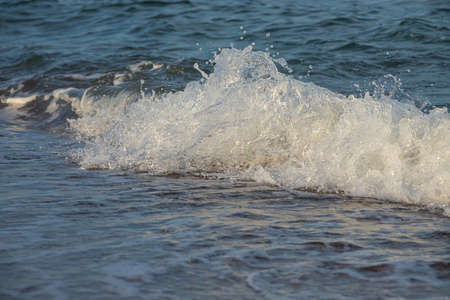 Sea waves crash against large rocks on the shore, forming large splashes..