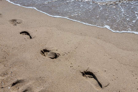 Footprints of a man on the yellow beach sand from walking barefoot by the sea with water that washes away the footprints. Contemplation of lifeの写真素材