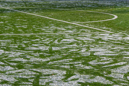 The football field with artificial green grass is covered with a light layer of snow. early spring. Green grass on the football field is visible from under the snow. amateur football field.の写真素材