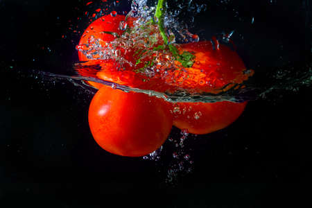 Fresh red tomato falling into water with water splash and air bubbles isolated on black background.