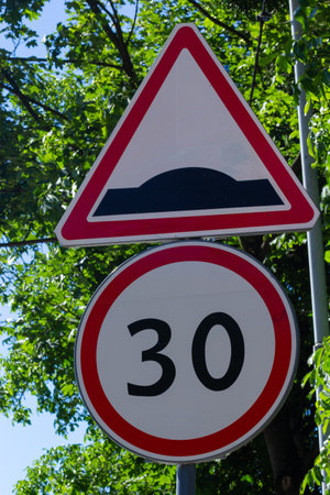 rough road sign and speed limit on a background of green trees and blue sky.の写真素材