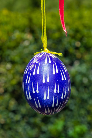 Painted eggs hang from the branches of the Easter tree. The focus is on a yellow egg painted by...