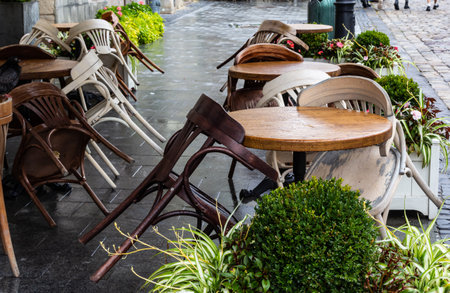 Empty wet wooden table and chairs on terrace of outdoor cafeteria during rain. Street city life in...