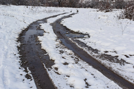 A country road through the forest, a wet road with snow falling from the trees.の写真素材