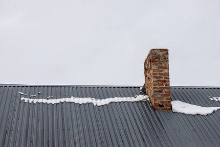a brick chimney on a metal roof in the winter under the snow. construction concept.の写真素材