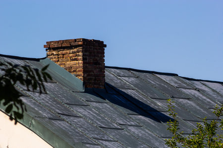 red brick chimney in the top of the village house. A roof made of tiles on the background of the sky.の写真素材