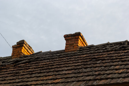 red brick chimney in the top of the village house. A roof made of tiles on the background of the sky.の写真素材