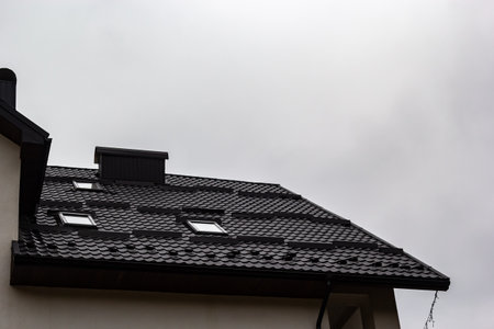 House with new brown metal tile roof and rain gutter. Metallic Guttering System, Guttering and...