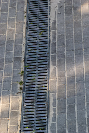 A lattice of a drainage paving system on a footpath made of square stone tiles, close up of a rainwater drainage system.の写真素材