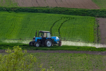 Aerial view of tractor spraying crop in green farm fields with pesticide.の写真素材