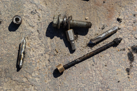 A collection of metal tools and fasteners is laid out on a rugged concrete surface. The items...