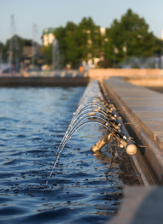 Water jets gracefully shoot up from the edge of a serene pool in Bucharest, Romania, illuminated by the warm glow of sunlight in the early evening.の写真素材