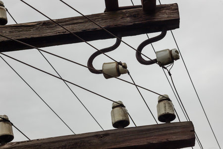 Overhead power lines support ceramic insulators, connecting utility poles under a gray, cloudy sky...