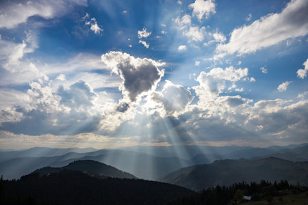 Sunlight streams through the clouds, illuminating the mountains below in a stunning display of nature's beauty during midday.の写真素材