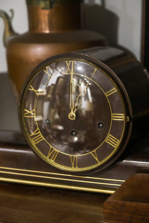 Close-up view of a vintage clock resting on polished wood. Roman numerals elegantly adorn its glass...