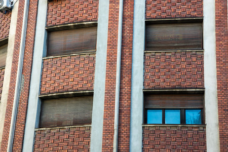 A brick building in Bucharest features a pattern of windows and shutters. The construction reflects...