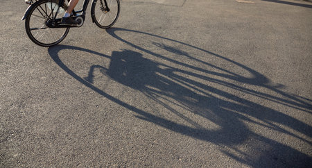 In the evening hours in Bucharest, a cyclist rides through a bustling area, while the warm light casts long shadows on the pavement, capturing the vibrant atmosphere.の写真素材
