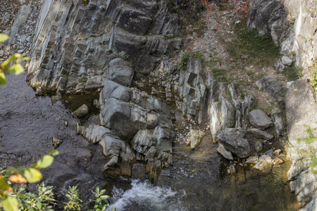 The scene captures uniquely shaped rocks beside a gentle river, surrounded by lush foliage, under...