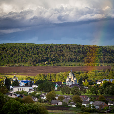 Clouds loom over a peaceful village surrounded by greenery and fields featuring a distinct church steeple captured on a late afternoon.の写真素材