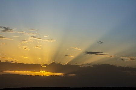 The sky showcases a brilliant display as the sun sets with golden rays streaming through clouds...