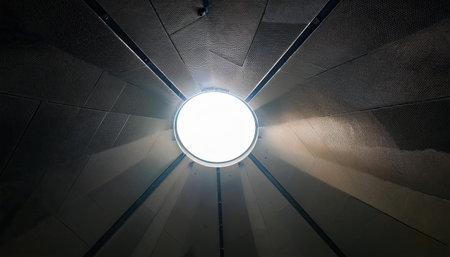 A blinding white light emanates from a circular opening in the ceiling tiles, creating a striking contrast against the dark surroundings below.の素材