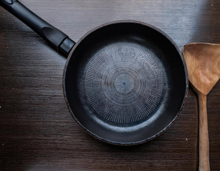 A classic black skillet rests on a smooth wooden surface, paired with a rustic wooden spoon. The arrangement highlights cooking essentials in a cozy kitchen setting.の素材