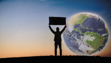 A silhouette of a person stands holding a sign with the message Save the Earth against a backdrop of a glowing globe. The image symbolizes environmental awareness and action.の素材