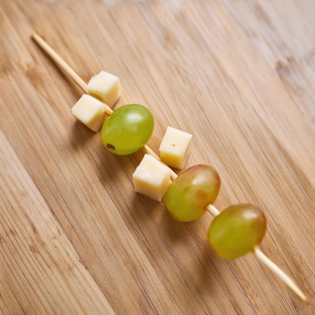 Colorful stick appetizer displays fresh grapes and cheese cubes arranged neatly on a wooden surface, perfect for parties or gatherings.の素材