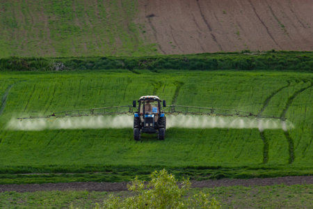 Aerial view of tractor spraying crop in green farm fields.